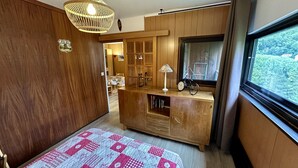 Una habitación acogedora con un armario de madera, una mesita con una lámpara, una bicicleta y vistas al exterior con zonas verdes.