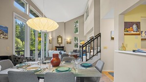 Comedor con una mesa dispuesta para cuatro, un jarrón grande y una escalera que sube a otro nivel.
