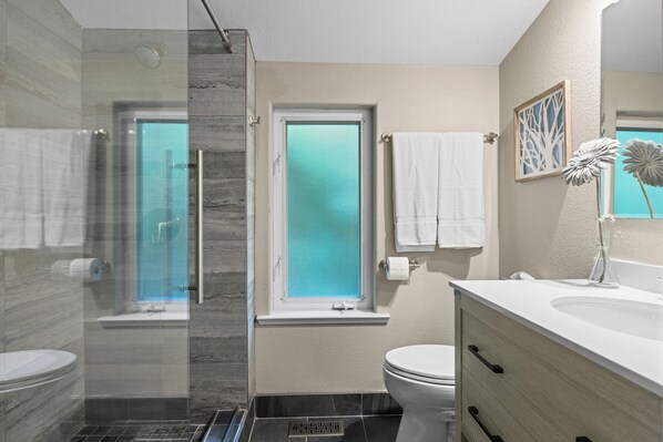 Een moderne badkamer met een douchecabine van glas, een toilet en een wastafelmeubel met een wastafel.