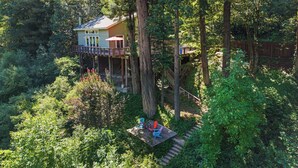 Una casa del árbol con terraza, rodeada de un bosque frondoso.