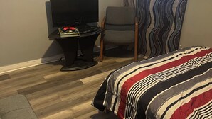 A bedroom with a bed, a chair, a small table with a TV, and a window with a wavy curtain. - Soothing 2-bedroom house with AC in charming 3 mins from Dearborn Hts (Inkster)