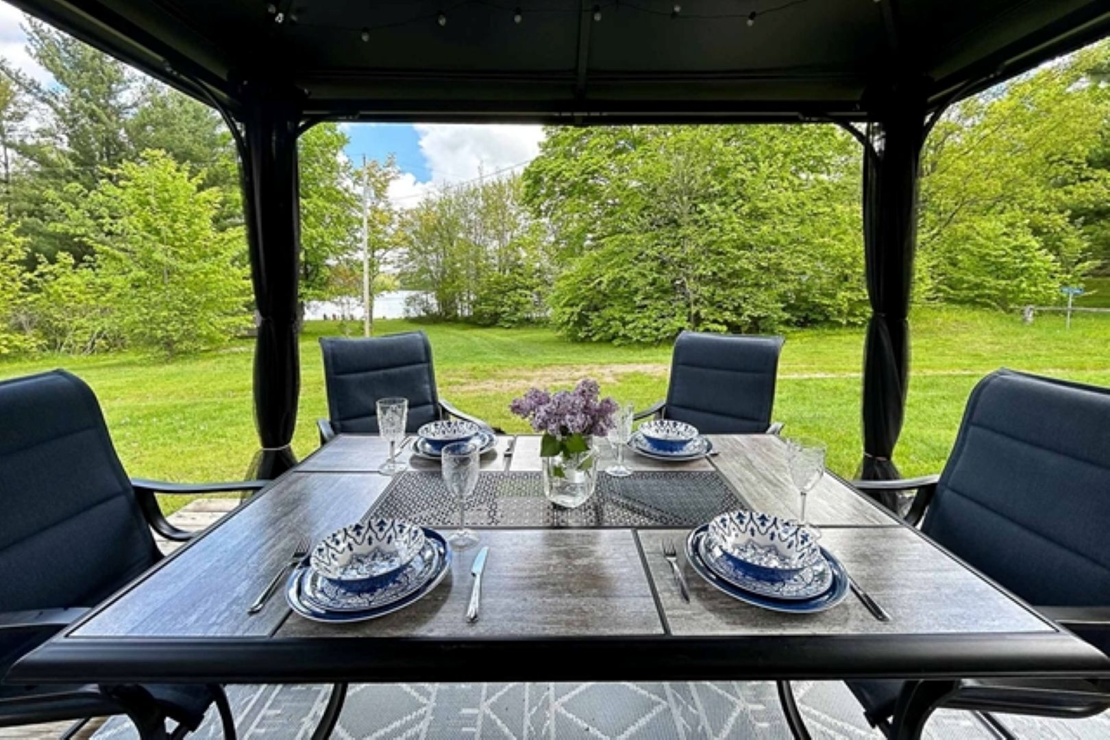 A table set for four with blue and white patterned plates, silverware, and a vase with purple flowers.