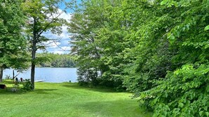 A grassy area with trees and a body of water. - Whimsical Waterside Cottage (Sharbot Lake)