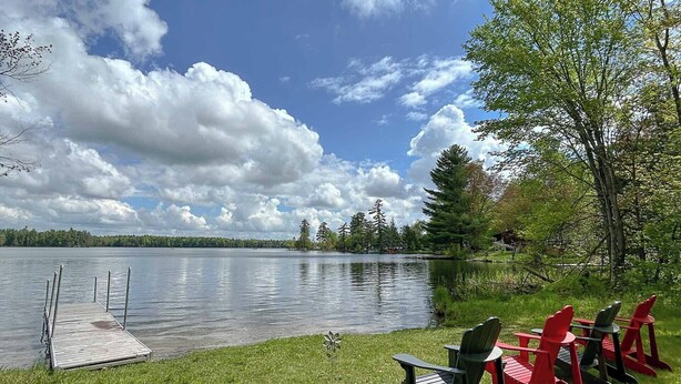 A lakeside view with a dock, chairs, and a grassy area. - Whimsical Waterside Cottage (Sharbot Lake)