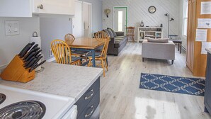 A kitchen with a dining area, a sofa, and a small table. There is a ceiling fan, a clock, and a window. - Whimsical Waterside Cottage (Sharbot Lake)