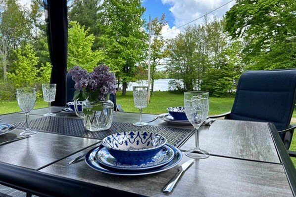 An outdoor dining table set with a blue and white bowl, wine glasses, and a pitcher of flowers.