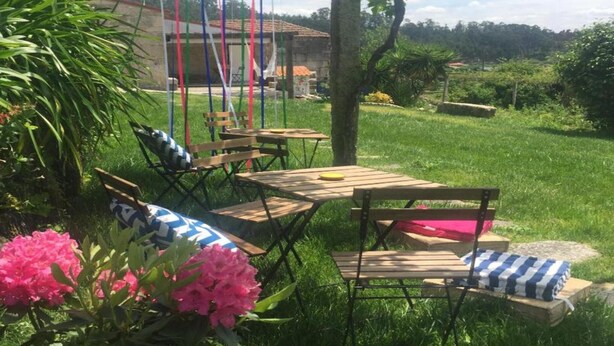 A garden with wooden furniture, a tree, and a building in the background. - Family Retreat at a Country House (Penafiel)
