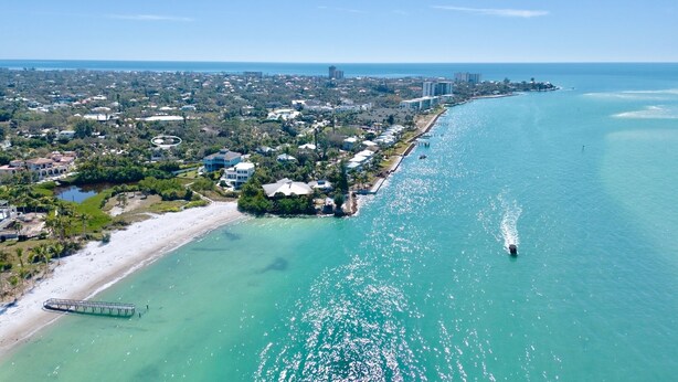 Luchtbeeld van een kustplaatsje met een strand, helder turquoise water en een pier.