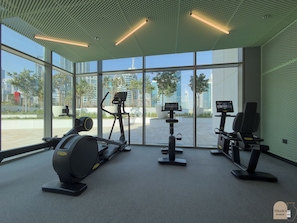 Ein modernes Fitnessstudio mit großen Fenstern, Trainingsgeräten und Blick auf eine Stadtlandschaft.