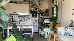 Una sala de estar acogedora con una mesa de centro de madera, un sofá blanco con un cojín azul, y un comedor con una mesa y sillas de madera.