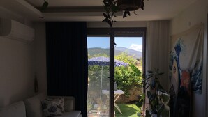 Una sala de estar con sofá, una mesita y un ventanal corredera que da a un jardín.