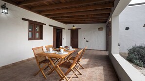 A patio with a wooden table and chairs, a tiled floor, and a white wall with a window and a door. - Home2Book Casa María Rustic Escape in Villaverde (Villaverde)