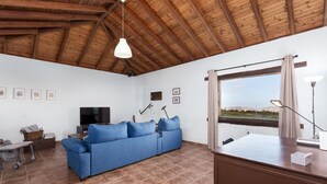 A spacious living room with a blue sofa, wooden ceiling beams, a large window with a view, and a flat-screen TV. - Home2Book Casa María Rustic Escape in Villaverde (Villaverde)