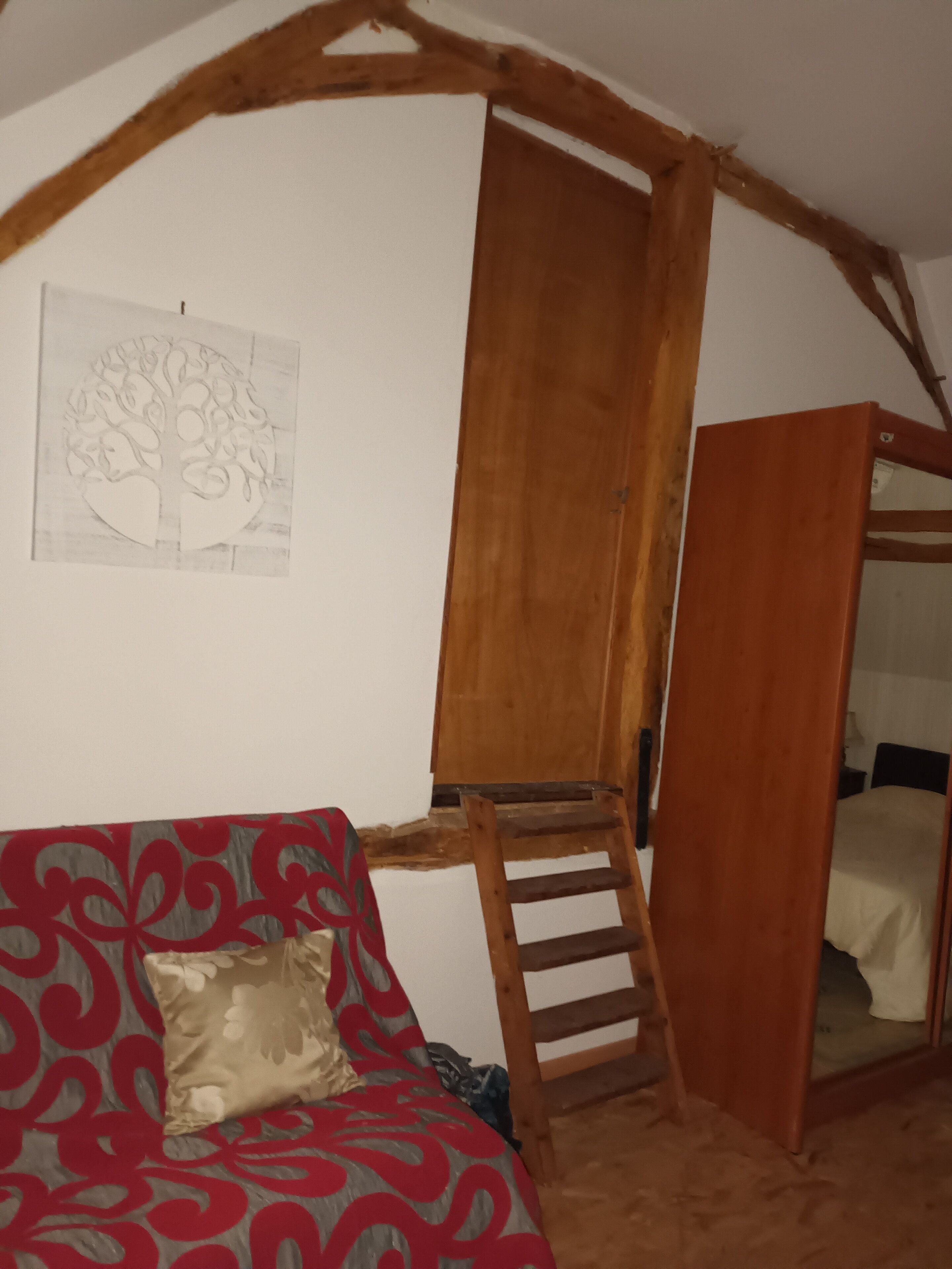 A room with a wooden ladder leading to a loft, a red patterned sofa, and a wall-mounted tree sketch.