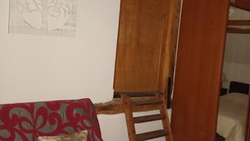 A room with a wooden ladder leading to a loft, a red patterned sofa, and a wall-mounted tree sketch.