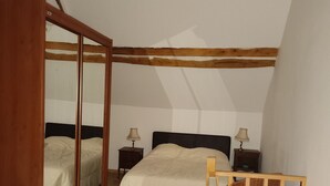 A bedroom with a bed, wooden headboard, two bedside tables with lamps, a wooden ladder, and a wooden floor.