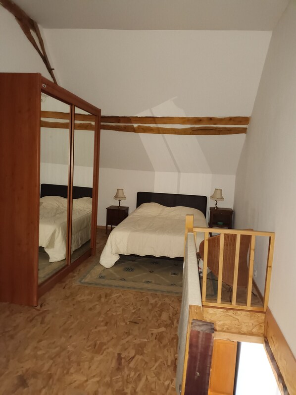 A bedroom with a bed, wooden headboard, two bedside tables with lamps, a wooden ladder, and a wooden floor.