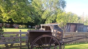A wooden wagon in a grassy area with a wooden fence and a building in the background.