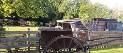 A wooden wagon in a grassy area with a wooden fence and a building in the background.