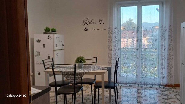 Un comedor con una mesa y sillas, un refrigerador y un ventanal con cortinas florales.