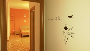 Un pasillo que conduce a un dormitorio con alfombra estampada, una cama y una pared con una firma y la silueta de un ave.