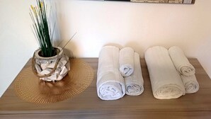 Una mesa de madera con toallas blancas enrolladas y un jarrón decorativo con plantas verdes.