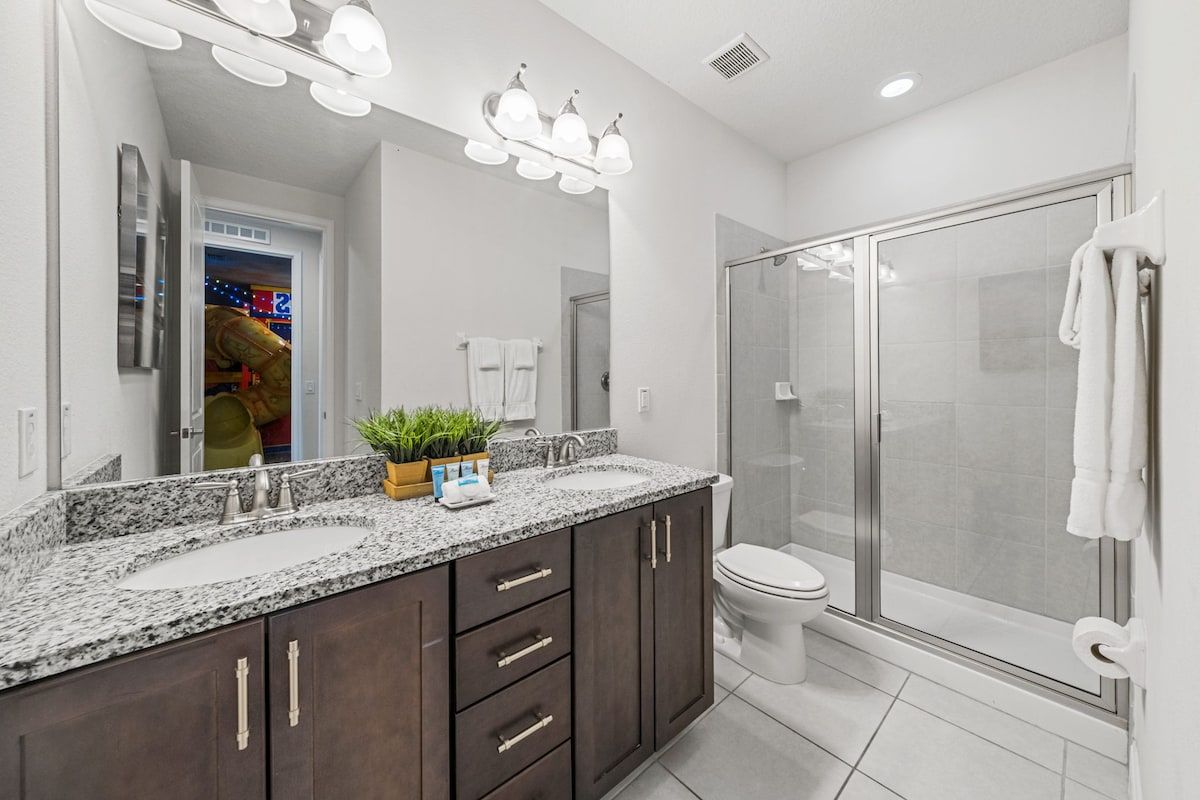A modern bathroom with a granite countertop, a glass shower enclosure, and a toilet.
