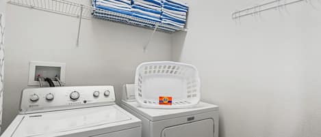 A laundry area with a Maytag washer and dryer, a white basket, and a shelf with folded towels.