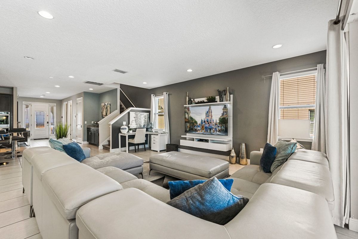 A modern living room with a large sectional sofa, a flat-screen TV, and a staircase leading to an upper level.