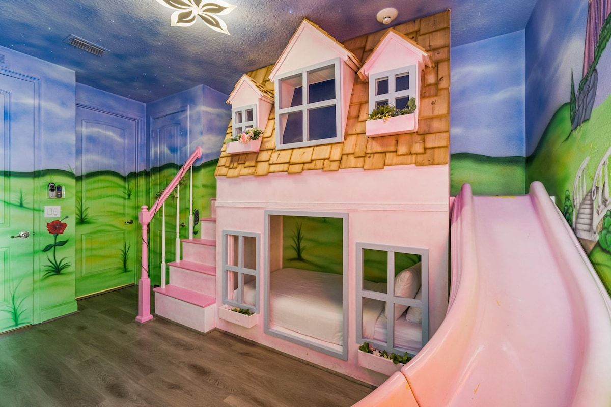 A children's playroom with a slide, a staircase, and a mural of a house.
