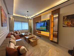 Una sala de estar moderna con un televisor de pantalla plana grande, un sofá, una mesa de centro y una planta decorativa.