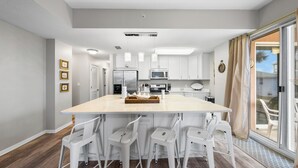 Una cocina moderna con armarios blancos, una isla central con taburetes y un puerta corrediza de vidrio al patio.