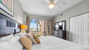 Habitación de hotel con una cama grande, ventilador de techo, televisión y puerta corrediza al exterior.