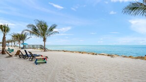 Uma praia com areia branca, palmeiras e um mar calmo.