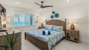 Um quarto com cama, ventoinha no teto, mesa de cabeceira, abajur, janela com persianas e uma planta.