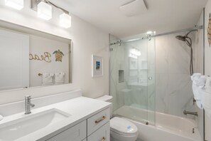 Een moderne badkamer met een glazen douchecabine, een wit wastafelmeubel en een toilet.
