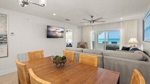 A dining area with a wooden table and chairs, a ceiling fan, and a view of the ocean through large windows. - Your Gulf-Front Getaway Awaits (Siesta Key)