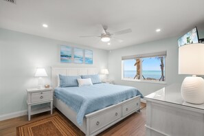 A bedroom with a bed, nightstands, a ceiling fan, a window with a view, and artwork on the wall. - Gulf-Front Serenity at Fisherman’s Cove (Siesta Key)