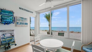 A room with a beach view, a ceiling fan, a white table with chairs, and a wicker chair with a blue cushion. - Gulf-Front Serenity at Fisherman’s Cove (Siesta Key)