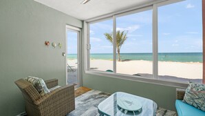 Ein Zimmer mit Blick auf den Strand, mit Korbmöbeln, Deckenventilator und Glastisch.