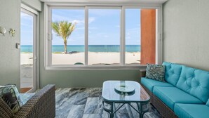 Ein Zimmer mit Blick auf den Strand, einem Deckenventilator, einer Couch, einem Tisch und einem Korbstuhl.