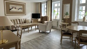 A living room with a sofa, armchairs, a coffee table, a TV, and a dining table with chairs. - Rein Klassik Hotel (Bad Pyrmont)