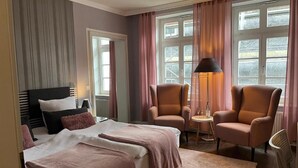 A hotel room with two beds, a sitting area with chairs, a lamp, and a view through large windows. - Rein Klassik Hotel (Bad Pyrmont)
