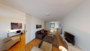 A modern living room with a sofa, coffee table, TV, and artwork on the walls. - BASELLODGING Schönau Serviced Living (Basel)