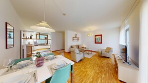 A modern living room with a sofa, a dining table set for four, and a TV. - BASELLODGING Schönau Serviced Living (Basel)