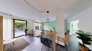 A spacious living area with a round table, several chairs, a sofa, and a large window offering a view of the outdoors. - BASELLODGING Schönau Serviced Living (Basel)