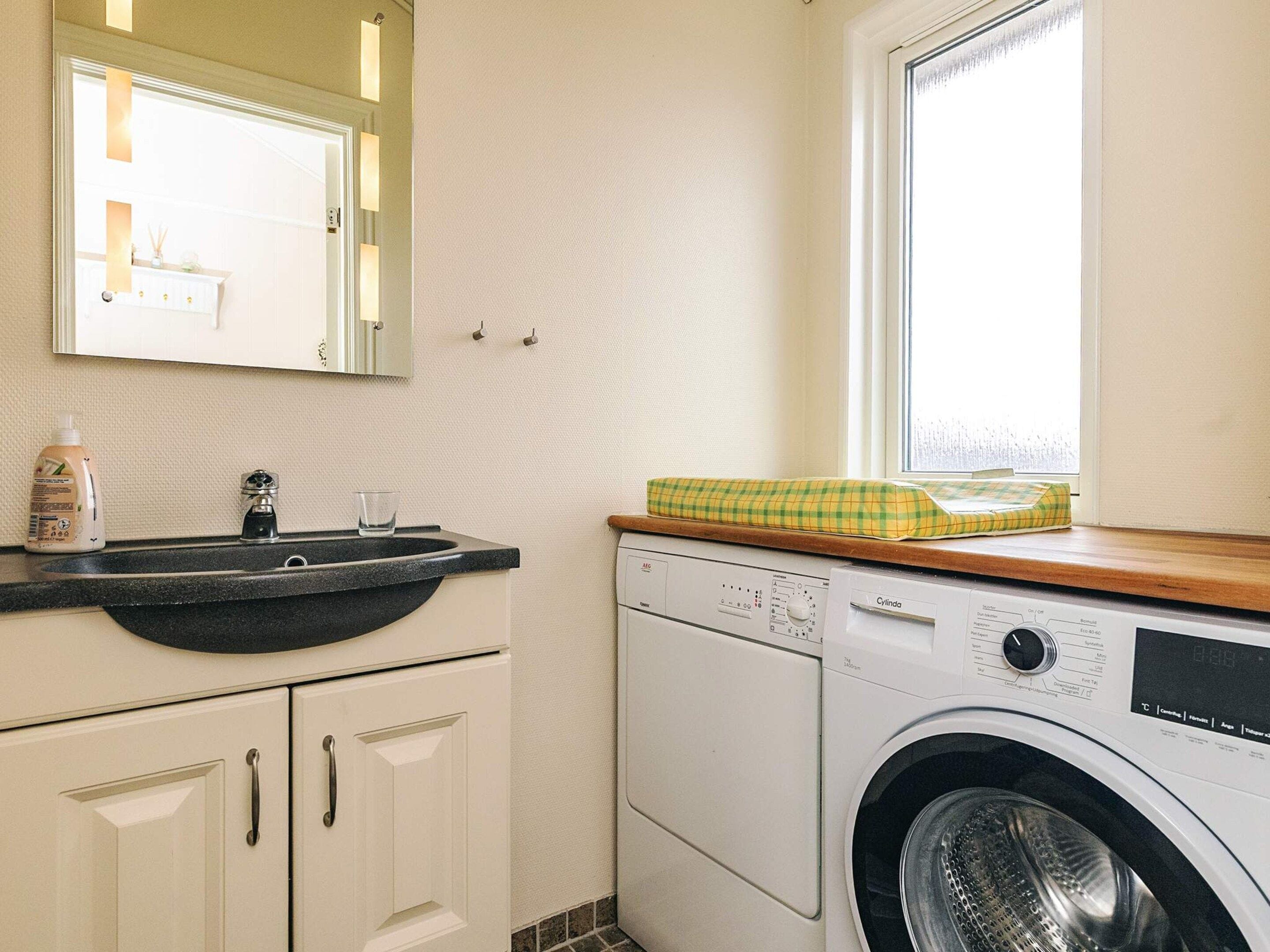 Een kleine wasruimte met een wasmachine, een wasbak en een spiegel erboven.