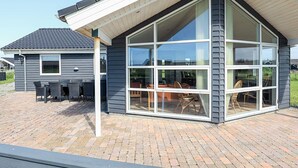 A modern house with a large glass window, a brick patio, and a covered outdoor seating area. - 5 Star Holiday Home in Lokken (Lokken)