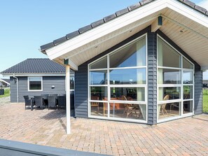 A modern house with a large glass window, a brick patio, and a covered outdoor seating area. - 5 Star Holiday Home in Lokken (Lokken)