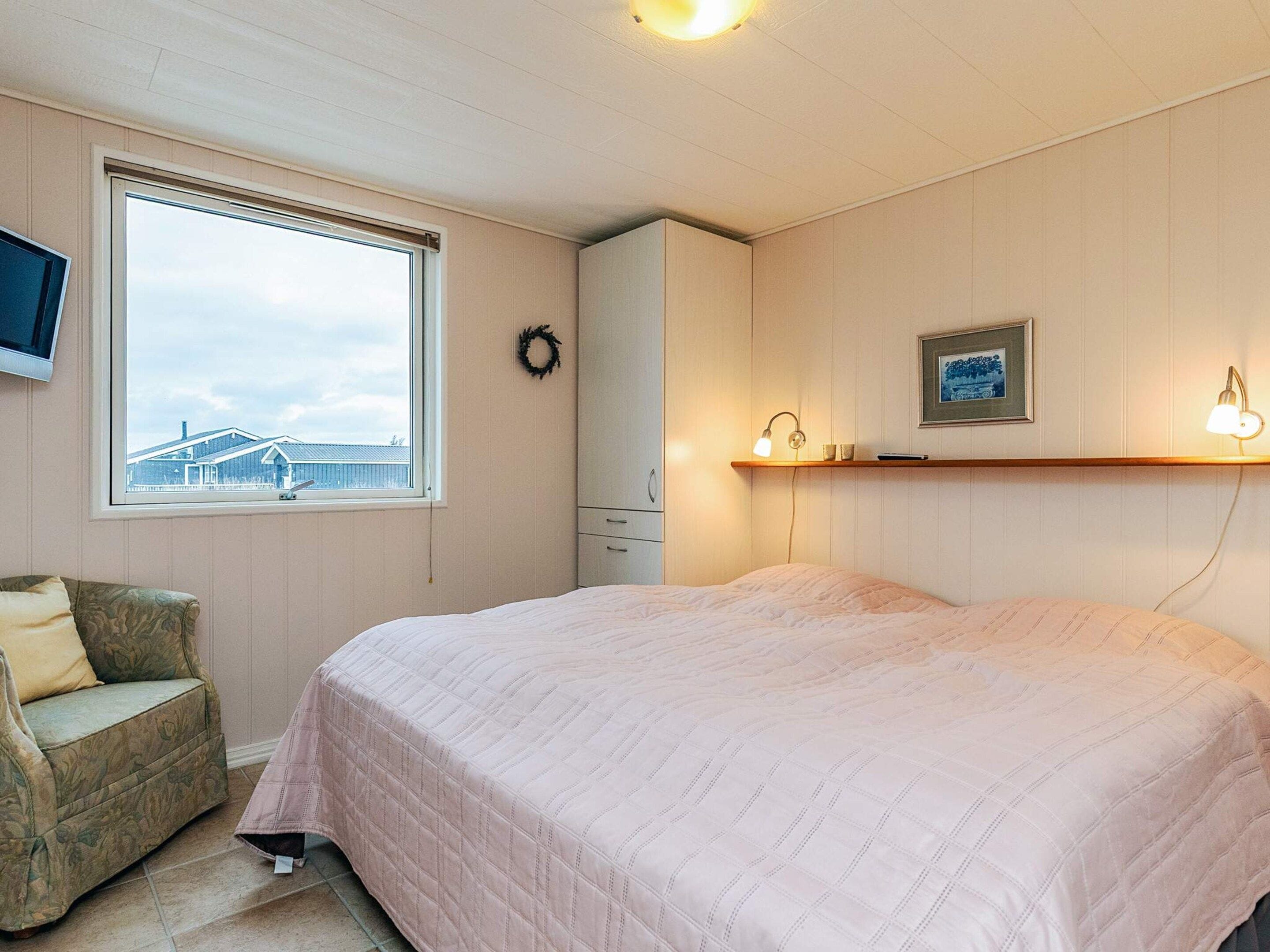 Een slaapkamer met een bed, een stoel, een kledingkast, een raam met uitzicht en een tv aan de muur.